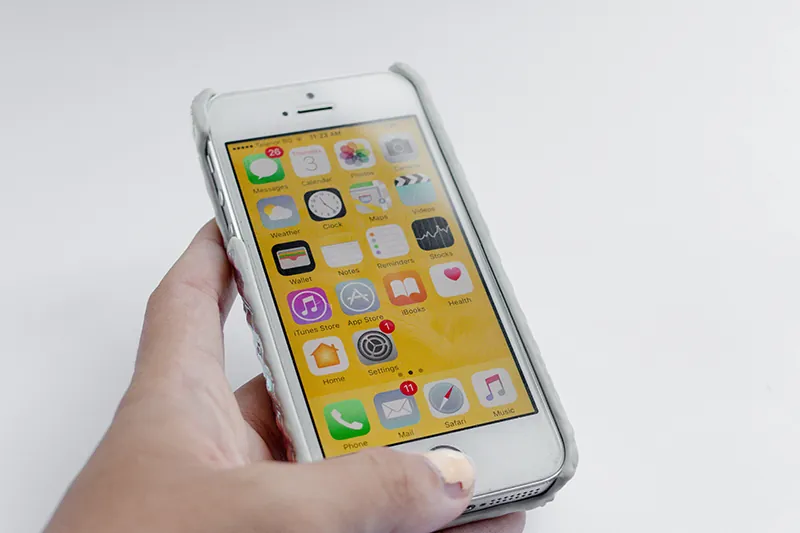 Dłoń trzymąjąca iPhone'a, na którego ekranie widoczne są liczne ikony aplikacji.