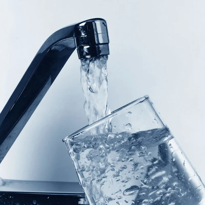 Water streams from a faucet into a clear glass.