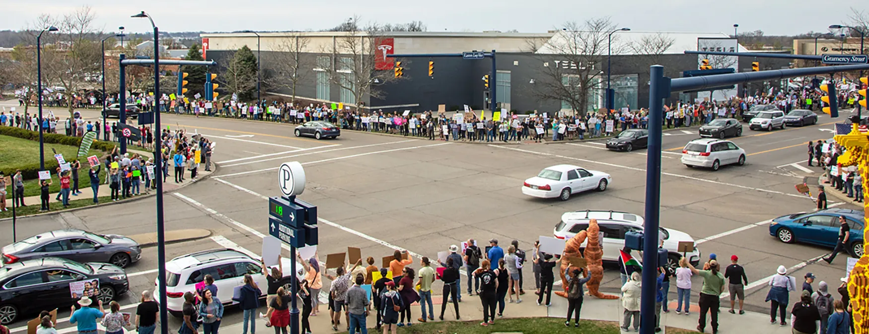 Protesters stand with signs on each corner of a large 4-way intersection.