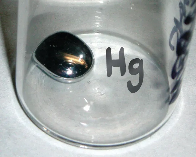 Se muestra un frasco marcado como "H g" con una pequeña cantidad de mercurio líquido en su interior.