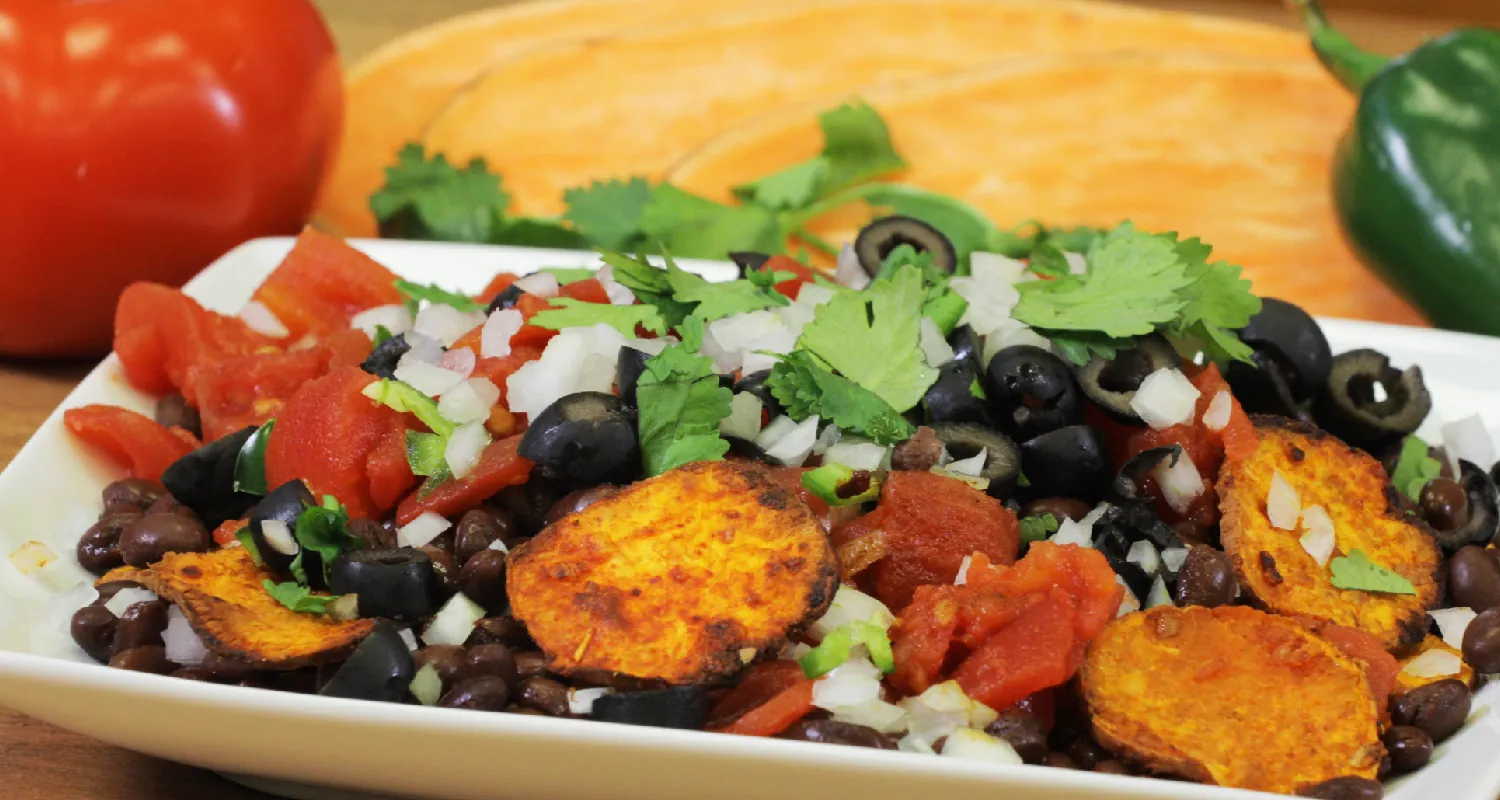 A plate of healthy nachos, consisting of sweet potatoes, black beans, red peppers, black olives, onions, and cilantro.
