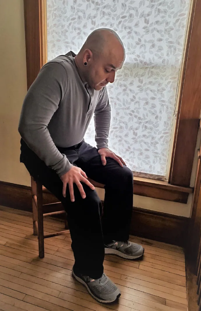 Man sitting on stool, bent over slightly with hands on thighs.