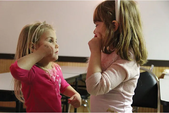 Image of two young girls signing to each other with their hands by their faces.