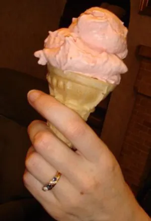 A woman holds a strawberry ice cream cone.