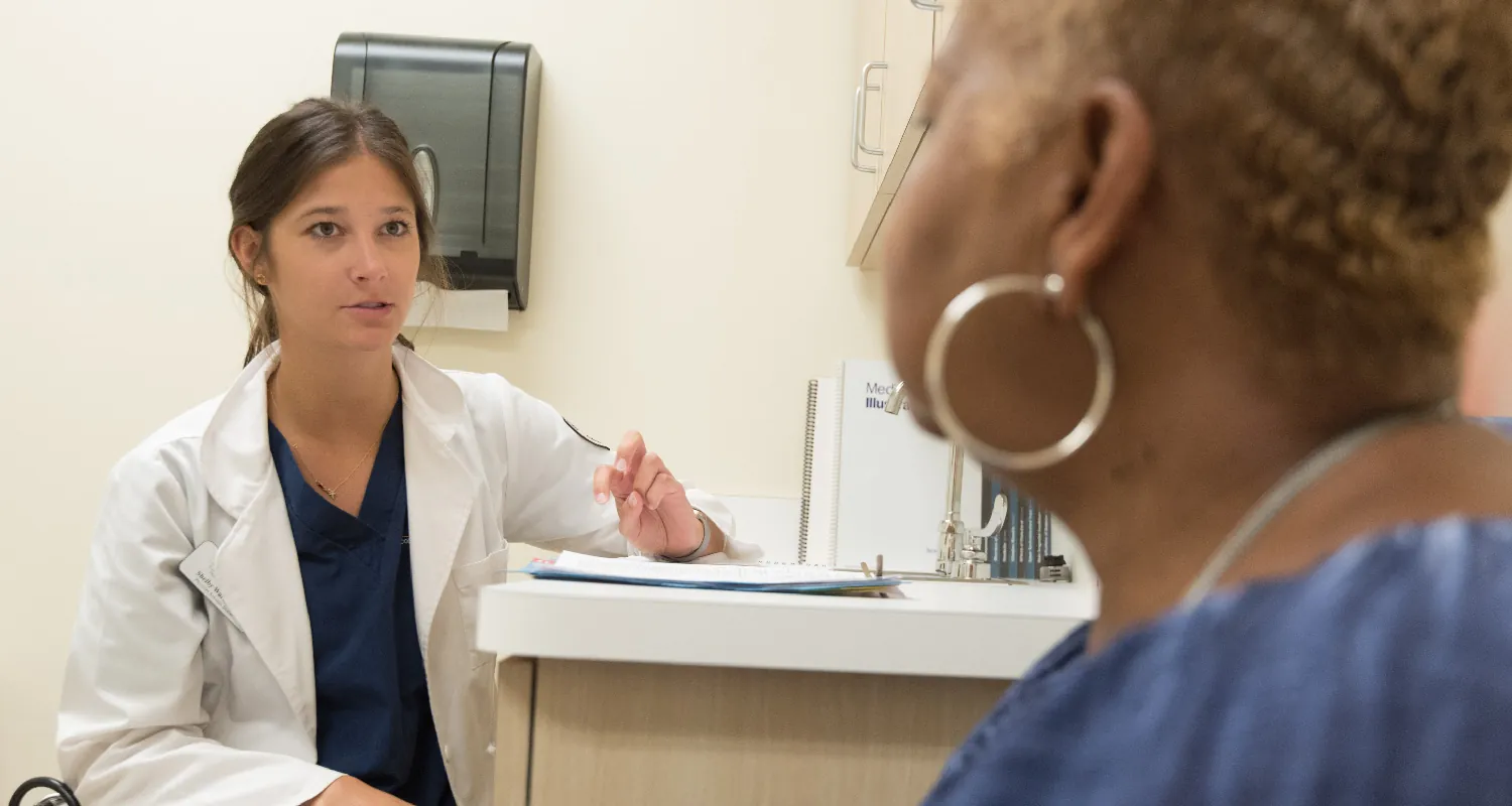 A healthcare provider sits at a counter in an exam room, speaking with a client who sits across from them.