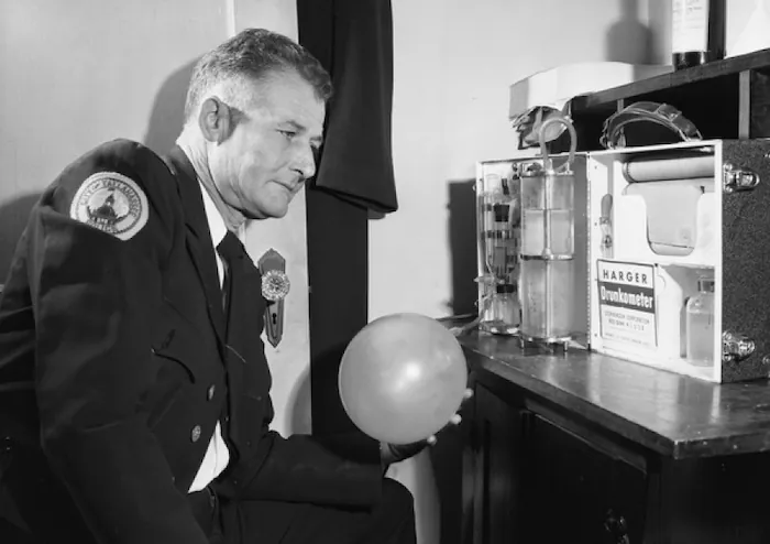 A photo of a police officer holding balloon that is connected to the Harger Drunkometer.
