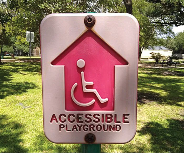A playground sign reading “Accessible Playground” and displaying a large arrow and person in wheelchair.