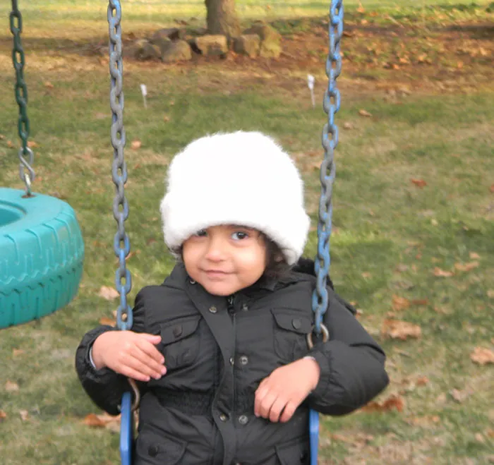 Photo of young child smiling while sitting on a swing.