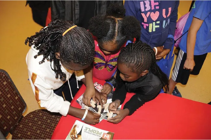 Image of three children huddled over a table, helping each other create items.