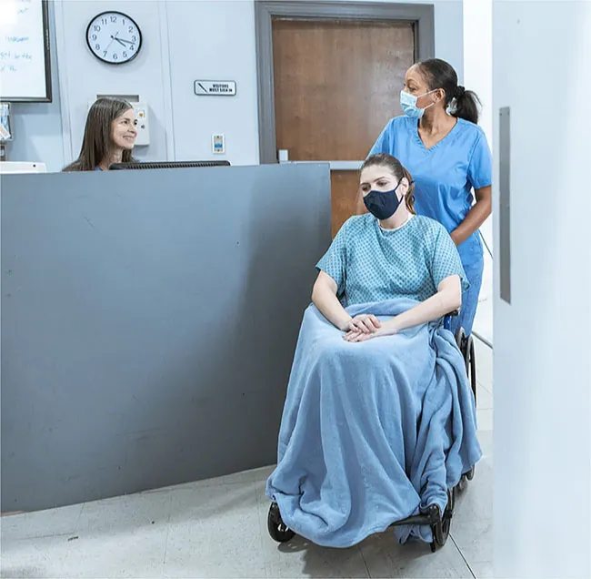 Healthcare provider pushing patient in wheelchair in admissions area.