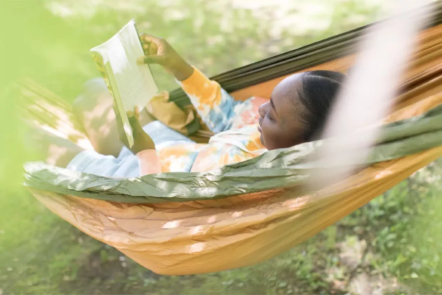 Photo of child reading a book in a hammock outside.