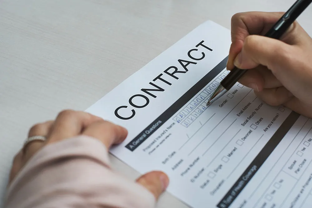A photo shows a closeup of a person signing a contract.