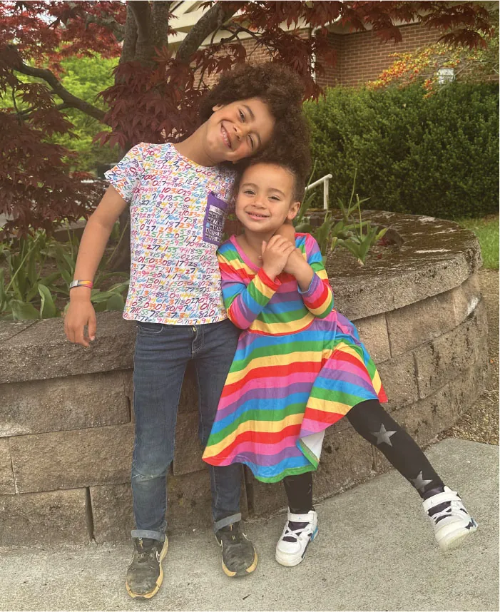 Photo of a three year old child being hugged by a six year old child (that is about a head taller than the three year old child).