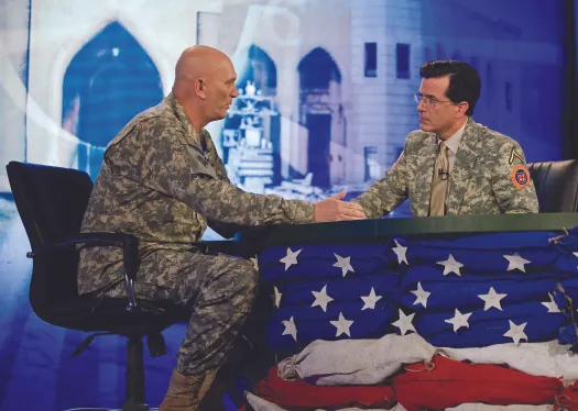 An image of Stephen Colbert and Ray Odierno seated on opposite sides of a table, facing each other.