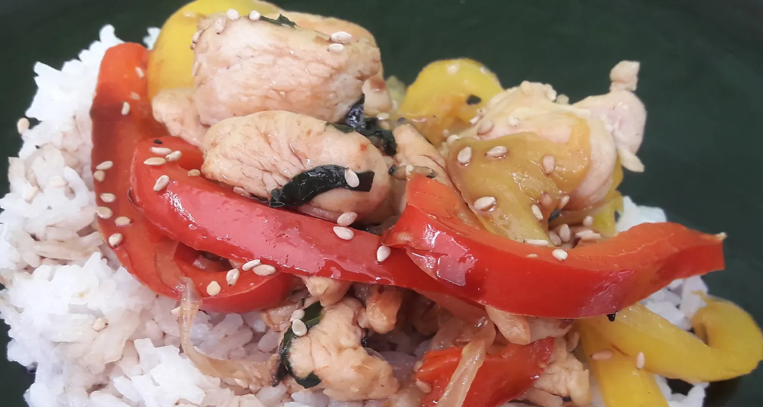 A serving of white rice with red pepper, yellow pepper, chicken, and sesame seeds on top.