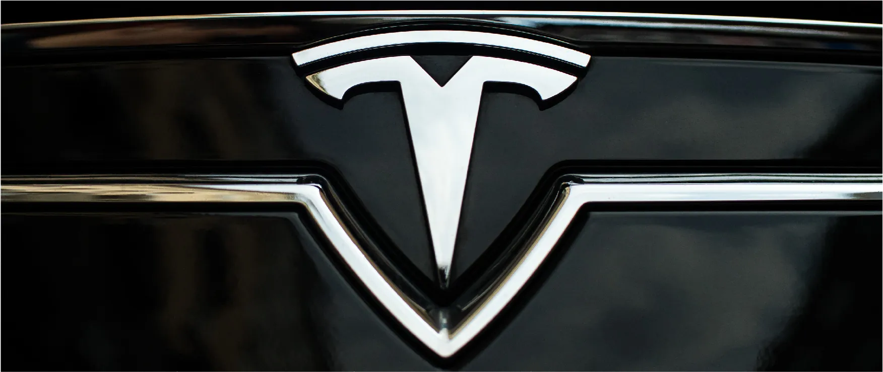 Close-up of a chrome Tesla logo on the front of a Tesla car.
