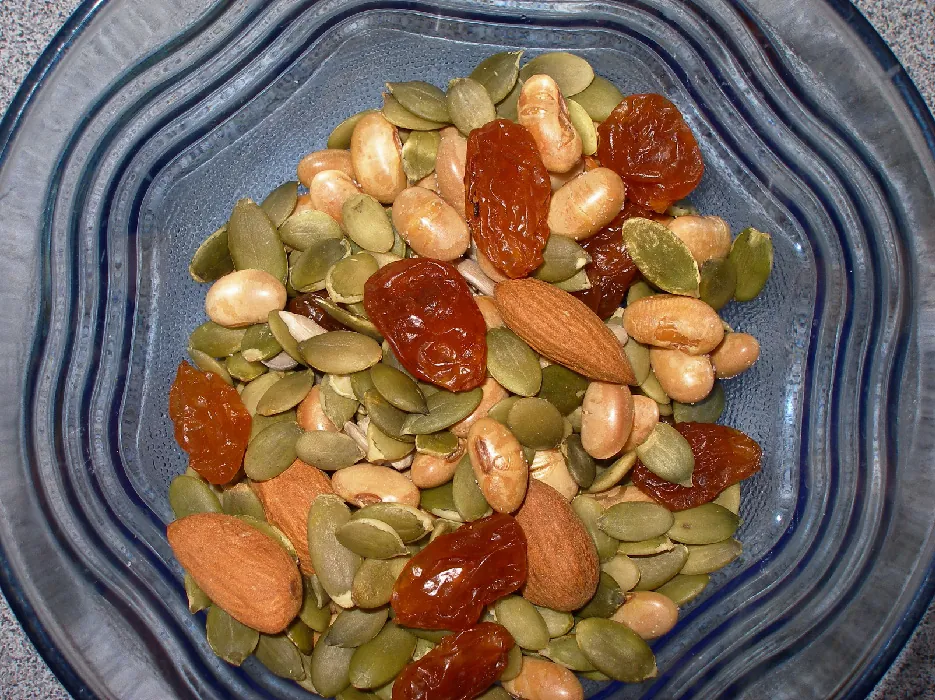 Almonds, green pumpkins seeds (pepitas), beans, and raisins in a glass bowl.