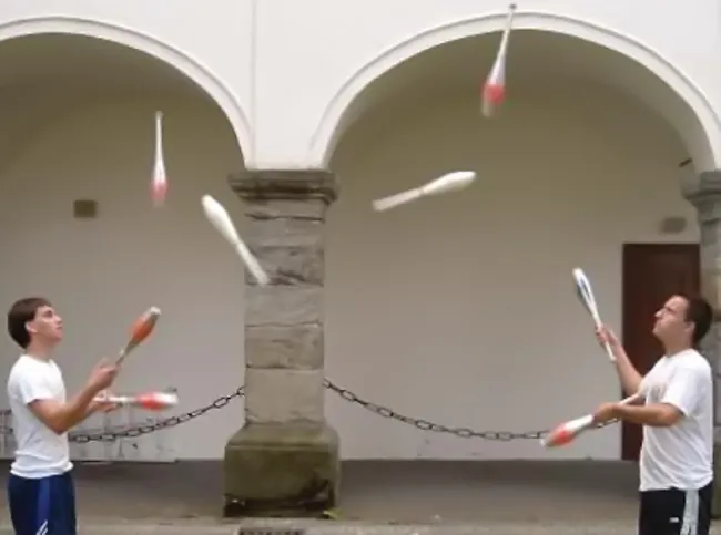 Se muestra a dos personas lanzando mazas de malabarismo de un lado a otro.