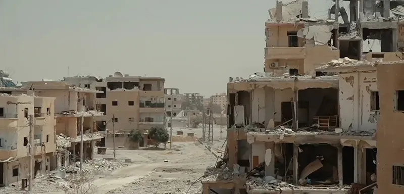 Destruction from the Syrian war included damaged buildings on both sides of an empty road.
