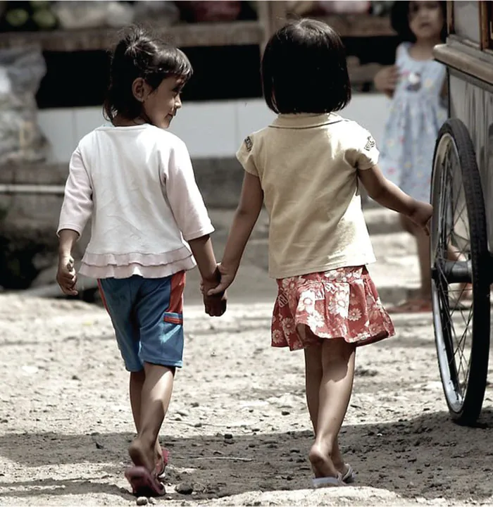 Photo of two young children walking hand in hand.