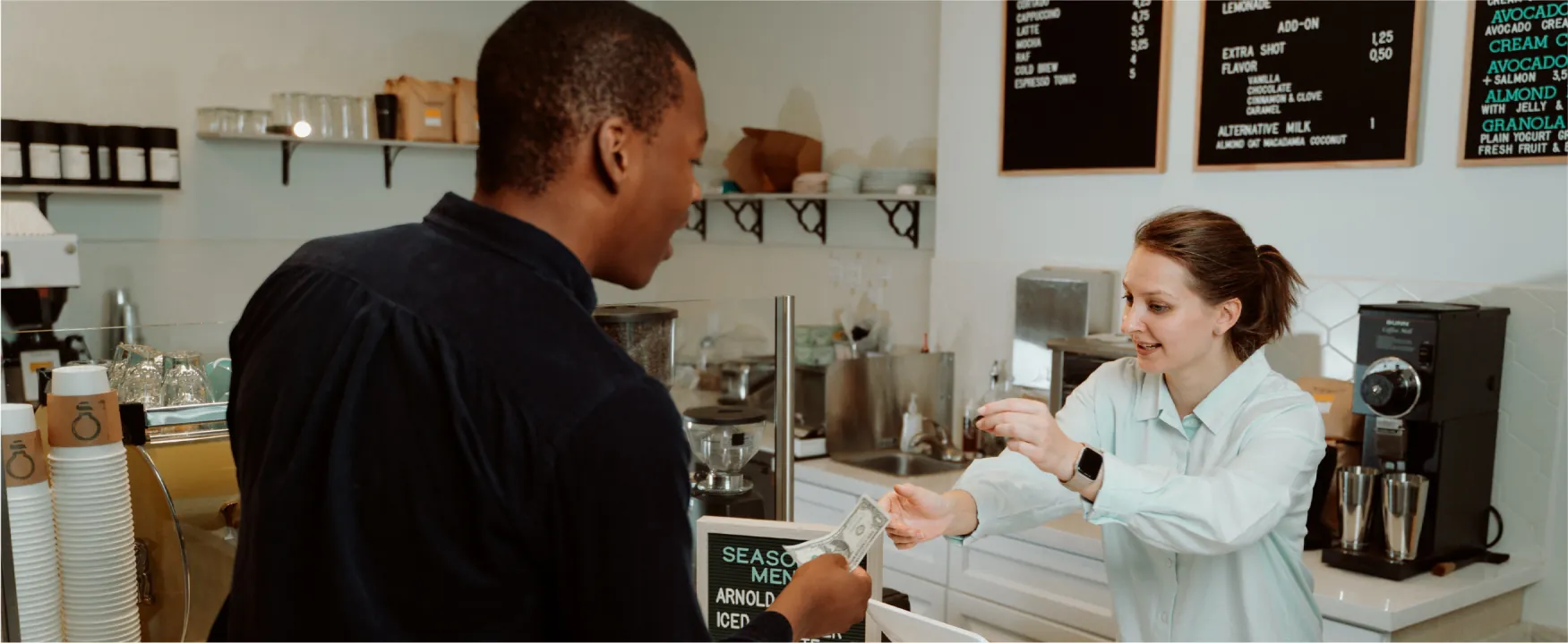 An employee at a coffee shop accepts payment from a customer. 