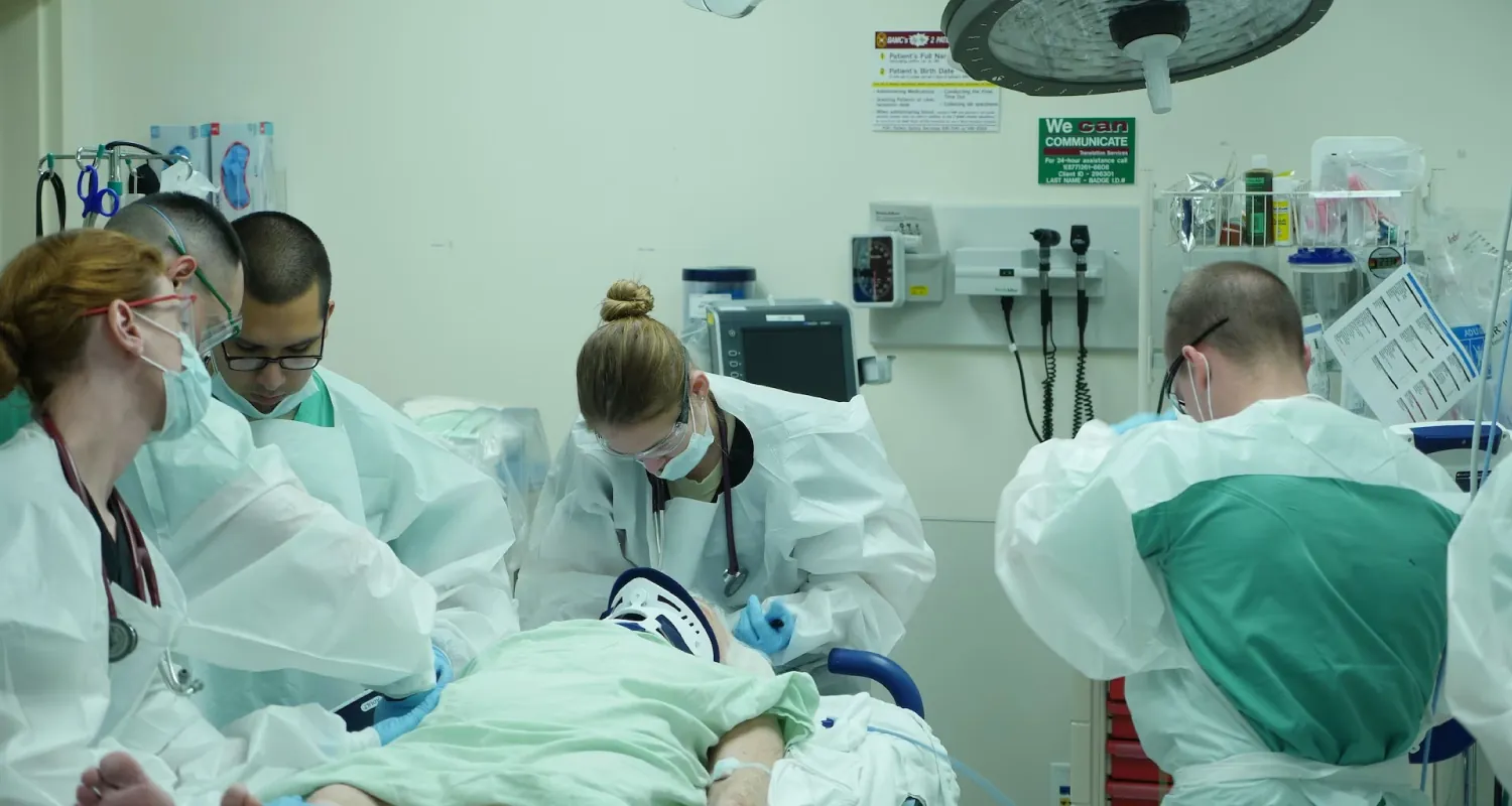 A medical team in protective gear surrounds a patient on a hospital bed, performing a procedure in an operating room.