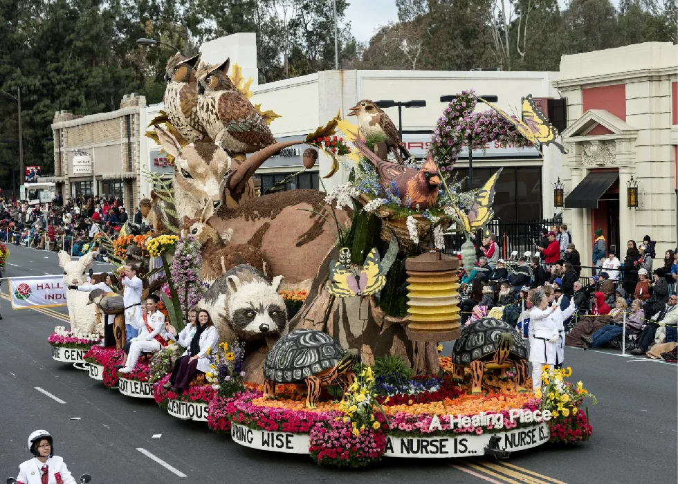 People wearing white lab coats ride on a parade float decorated with figures of forest animals and the words A Nurse Is . . . followed by various adjectives like Wise.
