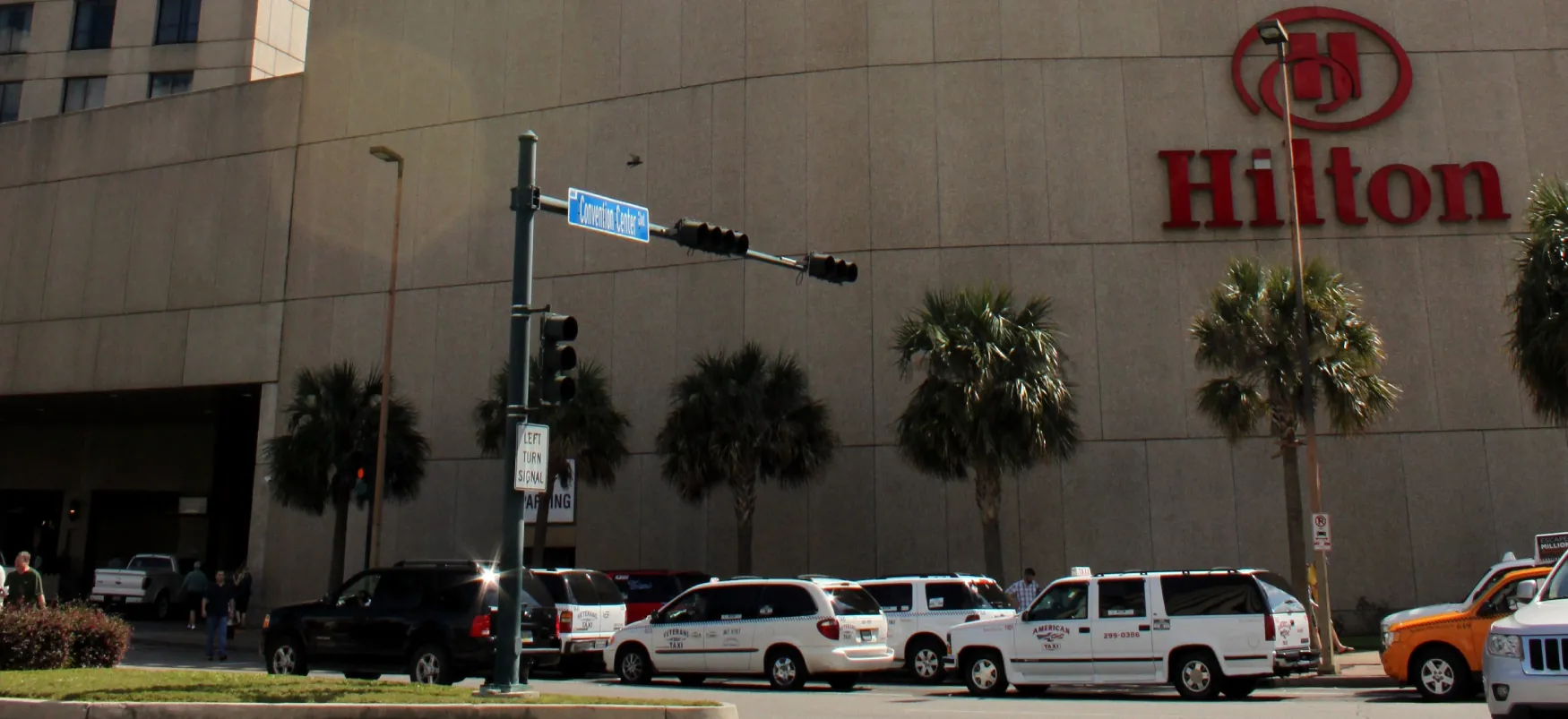 Cars and taxi cabs are parked in front of the Hilton Hotel façade. The Hilton name and logo are on the front of the building.