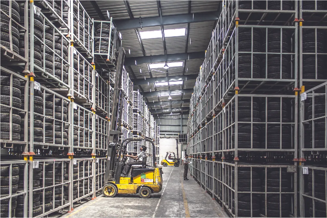 Photo of the inside of a tire warehouse, showing a forklift worker retrieving tires from a top shelf.