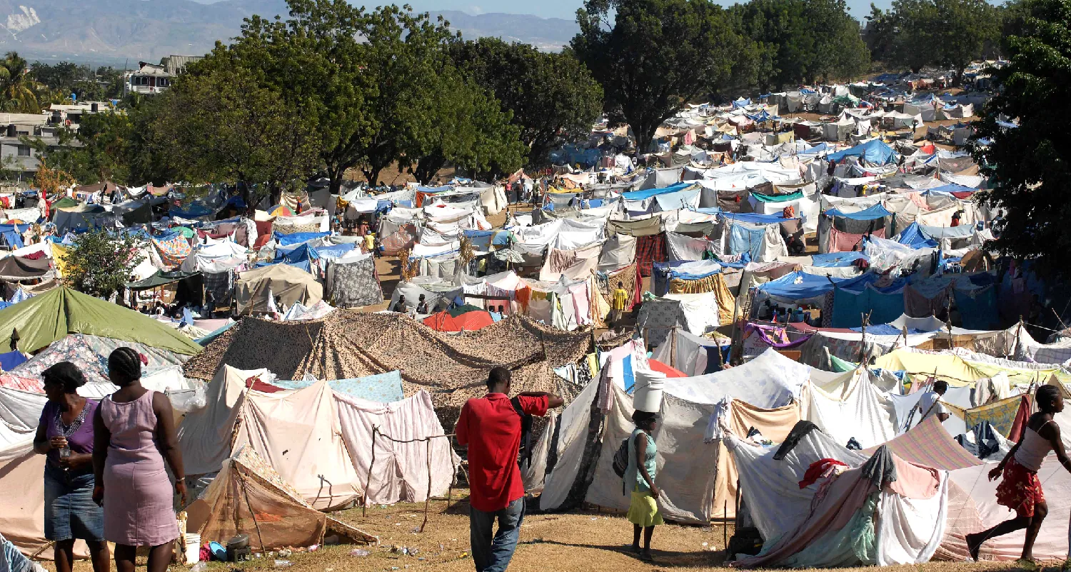 Color photograph of hundreds of tents. The tents are constructed of a variety of cloths of many different colors and are placed very close to one another. A handful of people are visible in the foreground of the image.