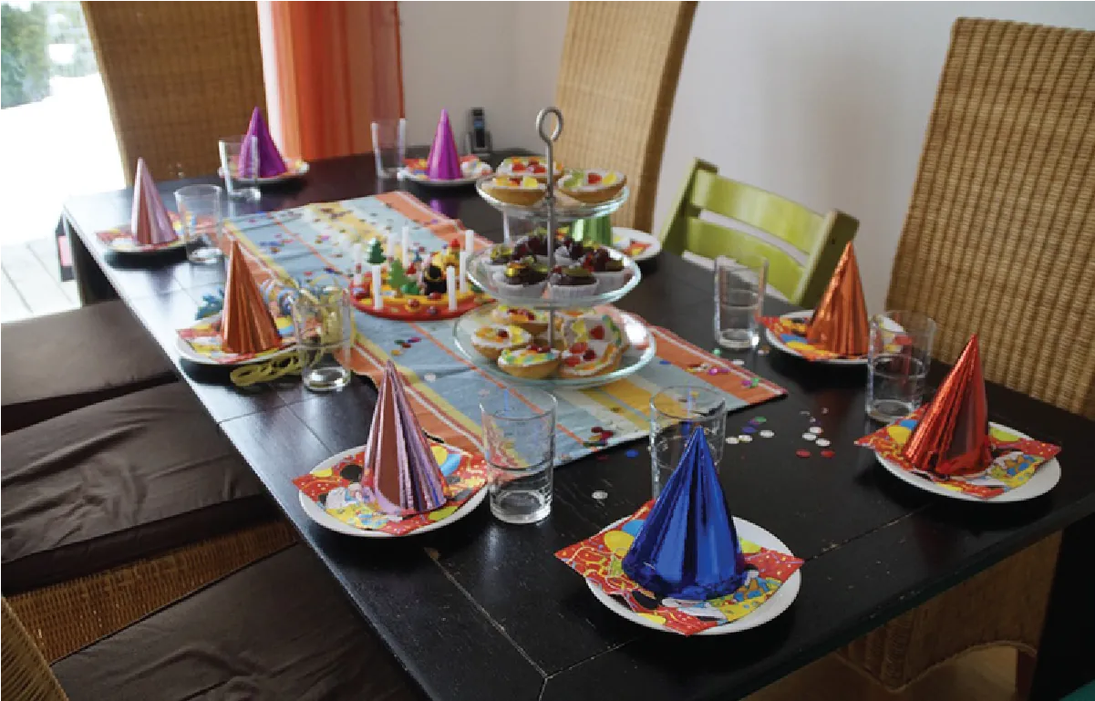 Photo of a table set for a party, with fancy party hats, napkins, and platters of cookies.
