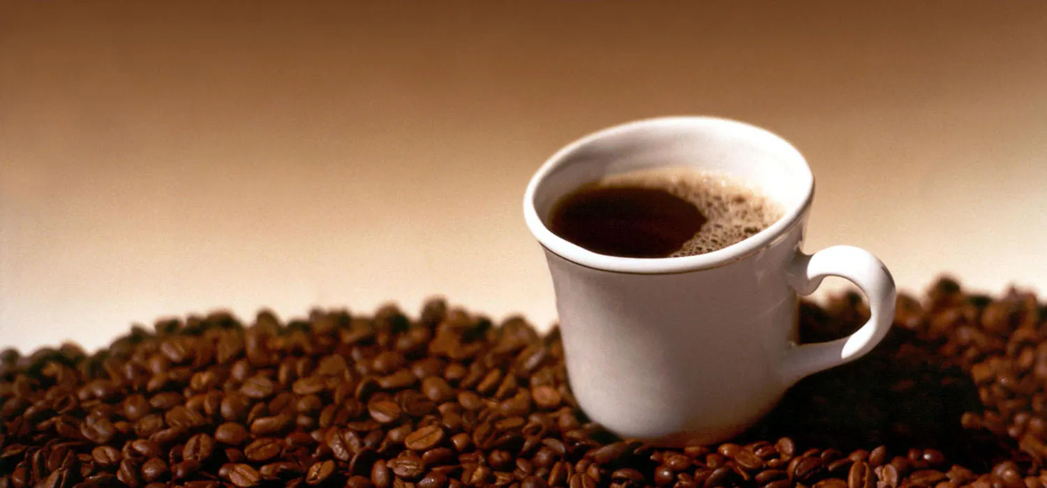A cup of coffee on a saucer in a tray of coffee beans.