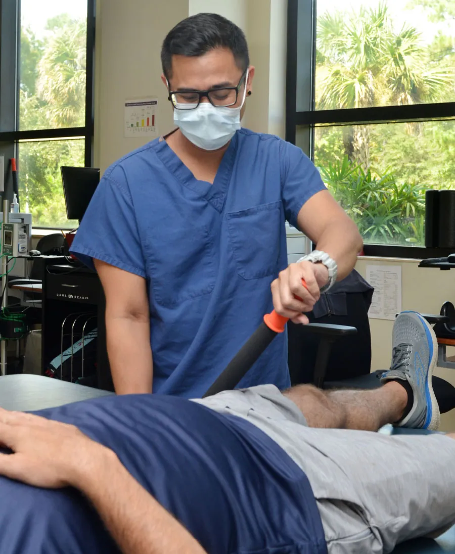 A color photograph shows a physical therapist using a therapy tool on the leg of his patient.