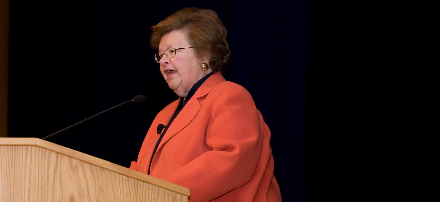 Senator Barbara Ann Mikulski speaks before a large wooden podium.