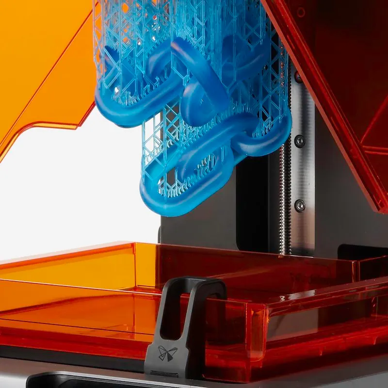 A group of oval chain links in the print bed area of the 3D printer. Connected to the chain links is an extensive lattice network of much thinner structures.