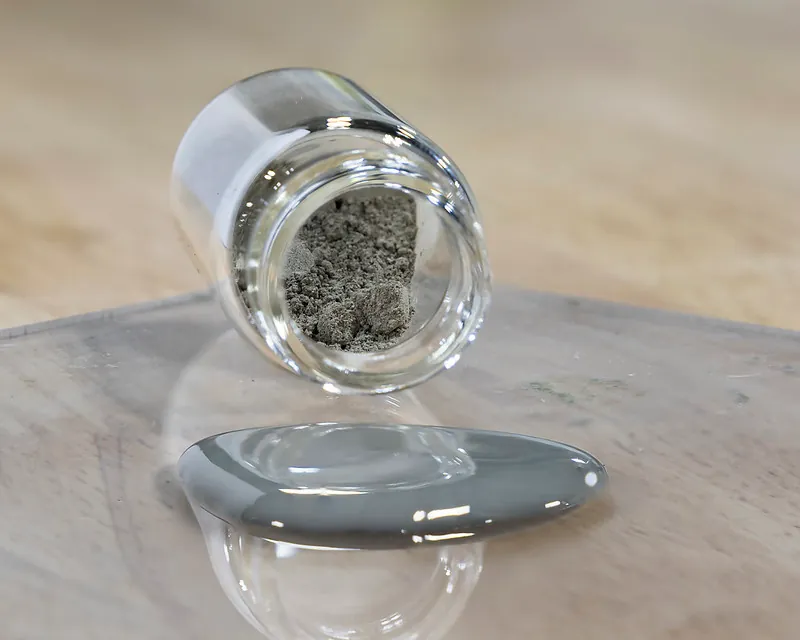 A small container of powder next to a small puddle of a metallic liquid.