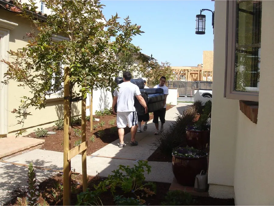 Photo of three individuals carrying a couch outside of a building.