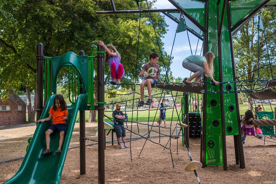 Photo of children playing at a park with adults looking on.