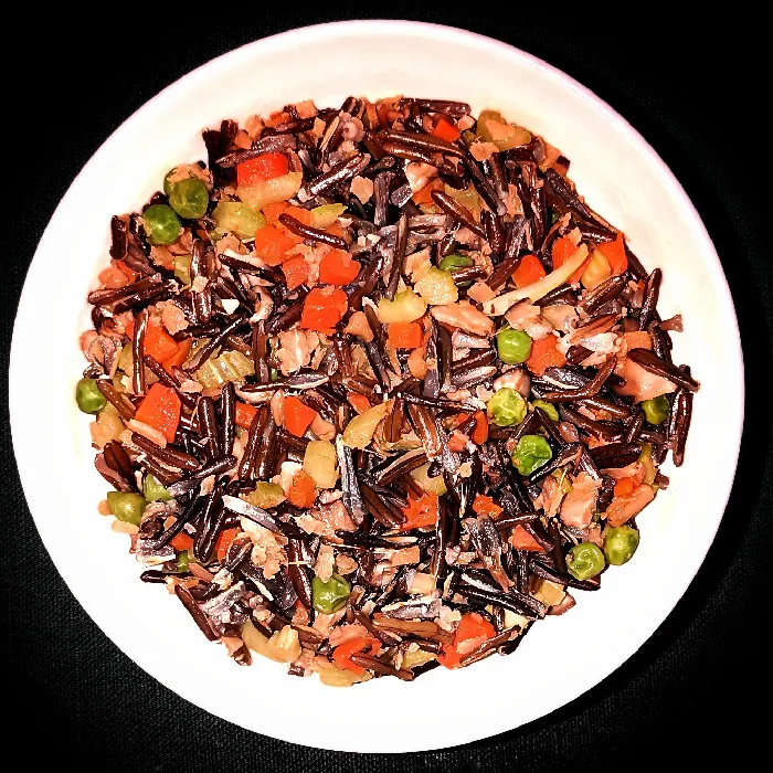 Cooked wild rice with bite-sized pieces of ginger, carrots, peas, and celery on a plate.
