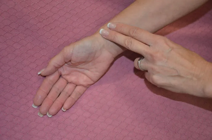 A photo of a woman palpating her radial pulse at her inner lateral wrist.