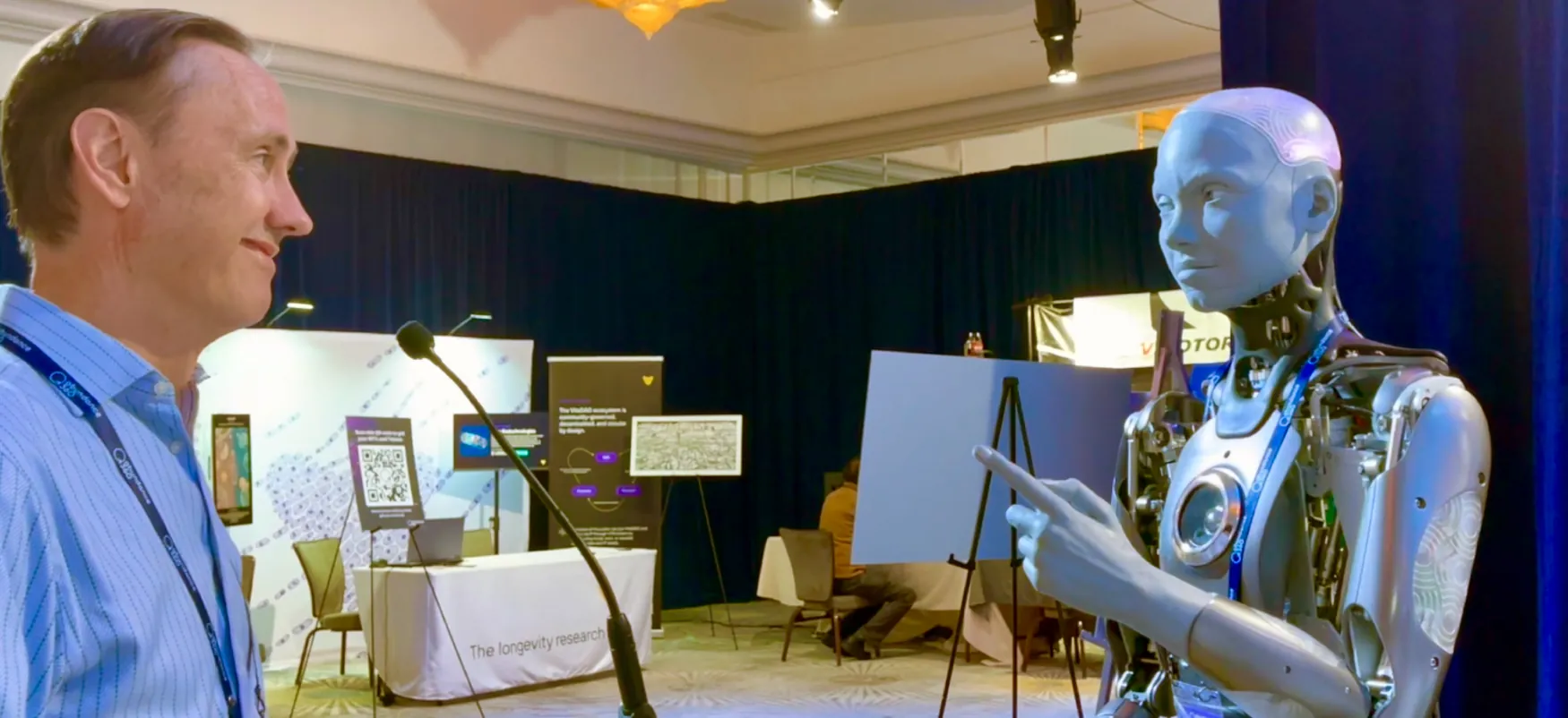 Person at a microphone “talking” to a humanoid robot at a trade show.