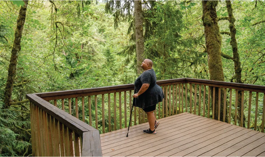 A person stands on a deck in a forested area.
