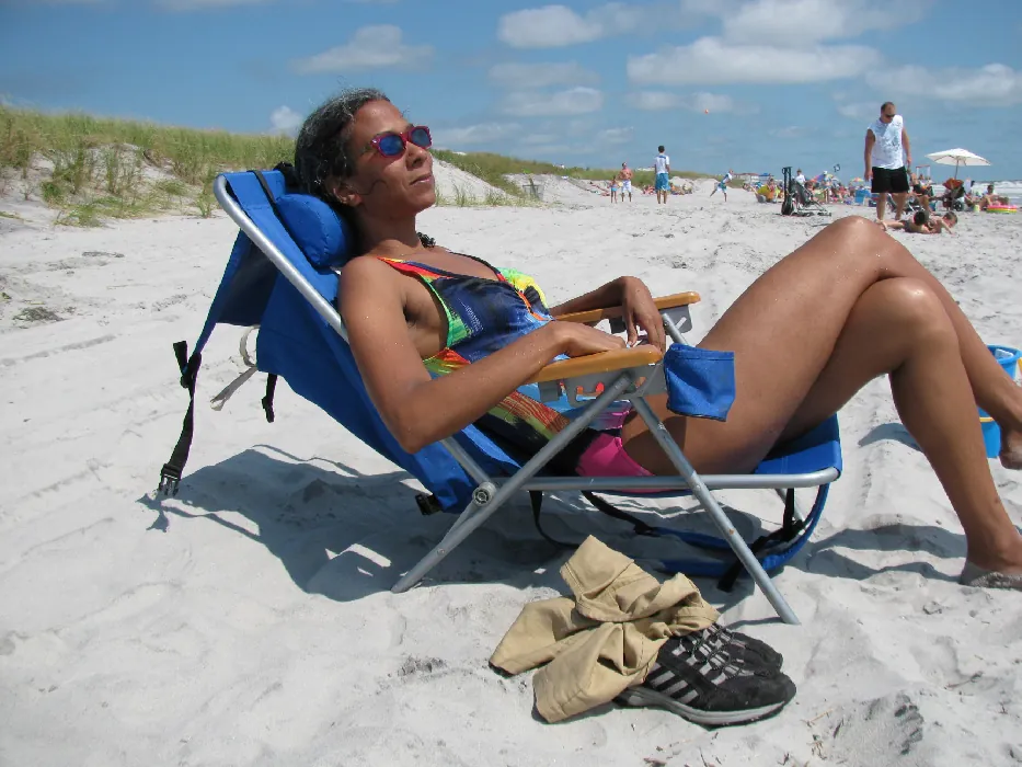 A person wearing a swimsuit and sunglasses sits in a chair at the beach.