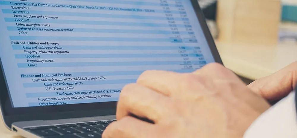 A close-up view shows the hands of a person typing on a laptop. The screen shows a budget.