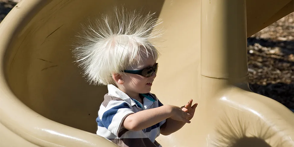 A photo shows a child sliding down a spiral-shaped slide, with his straight hair standing on end.