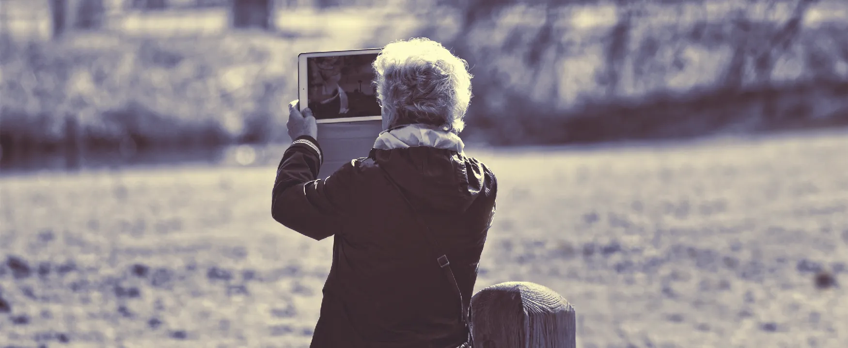 Picture of a person in a field by a stream holding up a computer tablet.