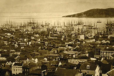 A photograph shows an aerial view of the port of San Francisco. The streets are crowded with houses, and the water teems with ships.