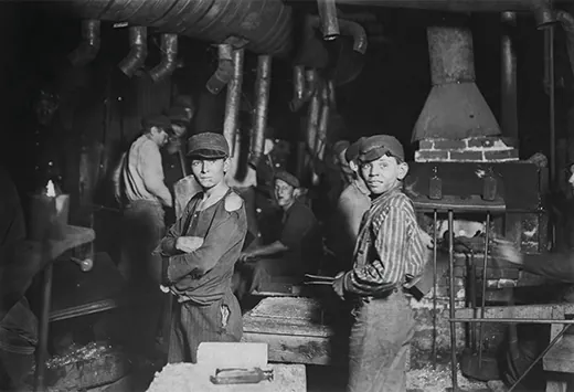A photograph shows a small group of children working in a factory. Two boys, with tattered clothes and dirt-smudged faces, stand in the forefront.