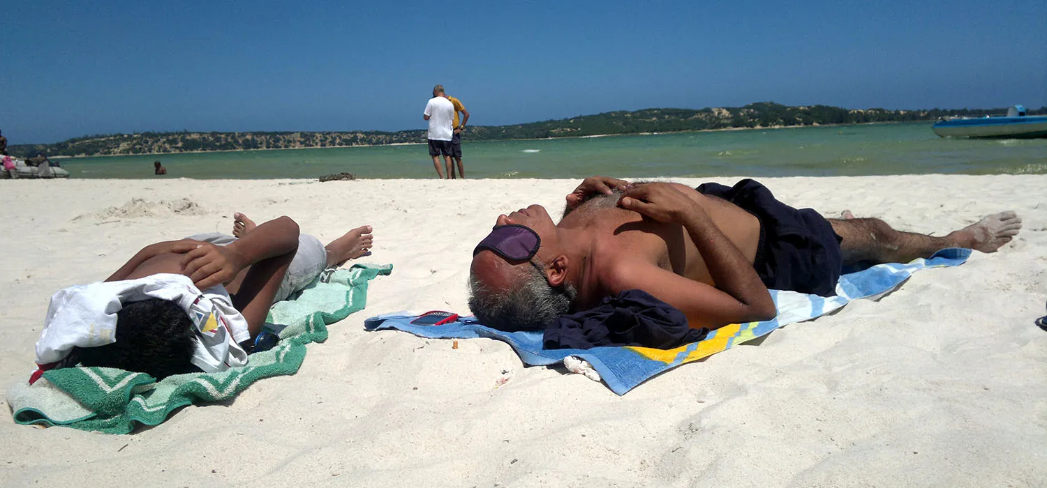 A photo of two sunbathers resting on the beach.