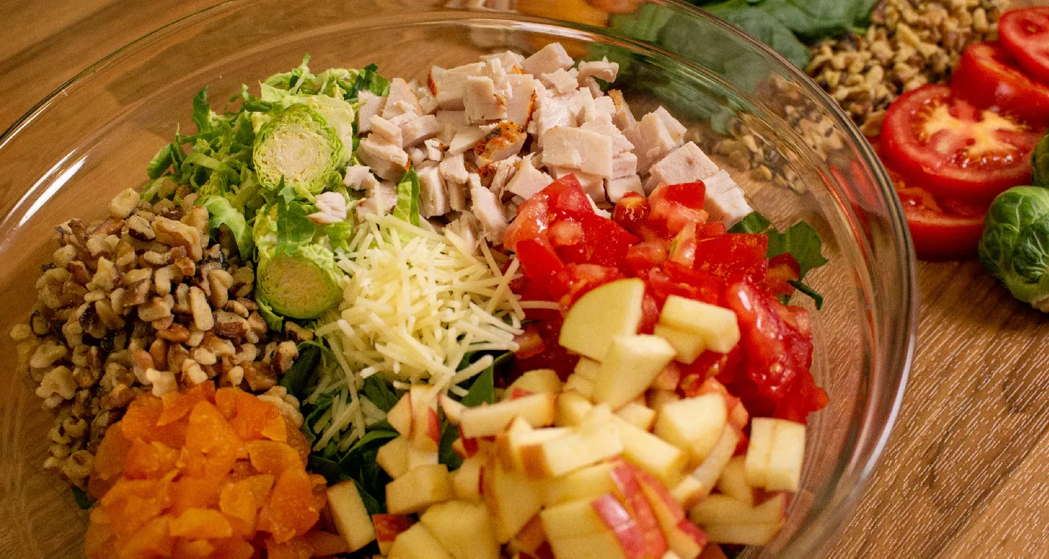 A bowl of chopped fruits, vegetables, and chicken, along with shredded cheese.
